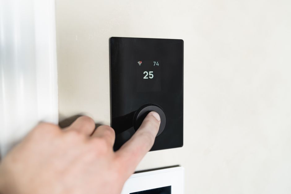 Homeowner adjusting a smart thermostat for heating and cooling